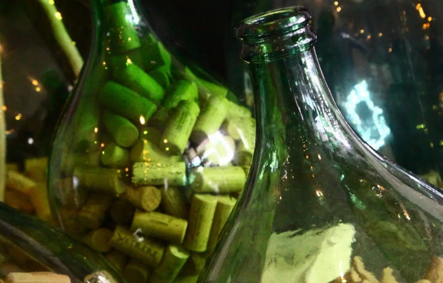 Damigiane di vetro verde piene di tappi di sughero, illuminate da piccole luci